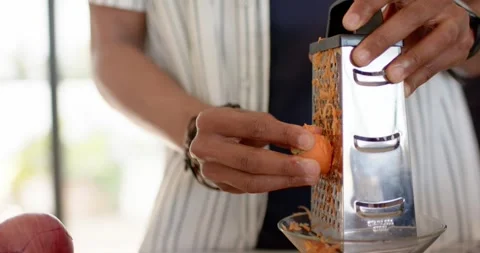 Upon grasping grater handle, hands are grating carrot at countertop, shredding Vidéo 342800315