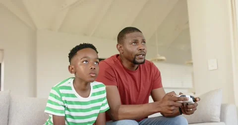 Upon second controller showing African American father and son gaming on sofa Stock Footage 340454374