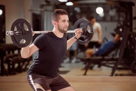 Upper body shot, squat exercise, young man holding barbell with weights on ba Stock Photos