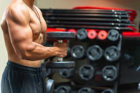 Upper body of an unrecognizable man lifting dumbbells in the gym Stock Photos