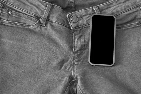 The upper part of old worn black jeans and a smartphone with a black screen Stock Photos