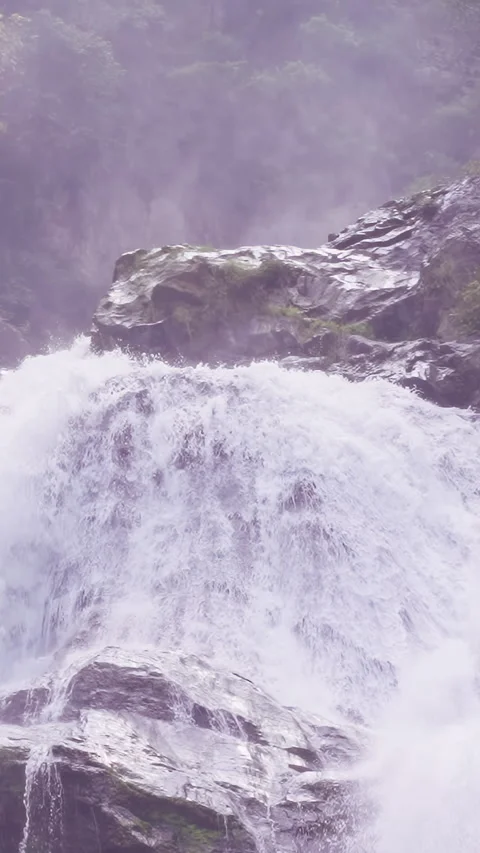 Upper section of waterfall pouring over rock ledge with mist and greenery formin 動画素材 328389143
