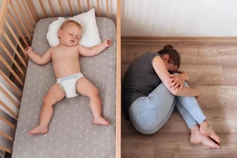 Upper view of baby napping in bed next to mother lying on floor suffering Stock Photos