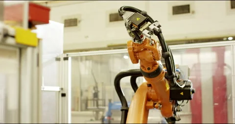 Upright orange robot arm turns at its station in a modern factory hall Stock Footage 331448814