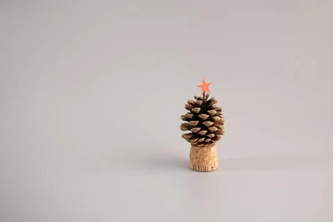 Upright pine cone with red star on cork base, solid light grey background, .. Stock Photos