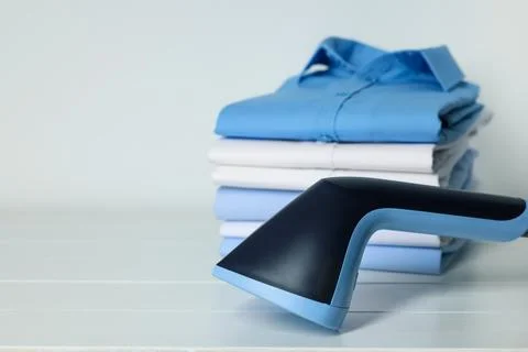 Upright steamer and stack of folded shirts on white wooden table, closeup. .. Stock Photos