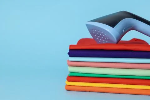 Upright steamer and stack of folded clothes on light blue background, close.. Foto stock