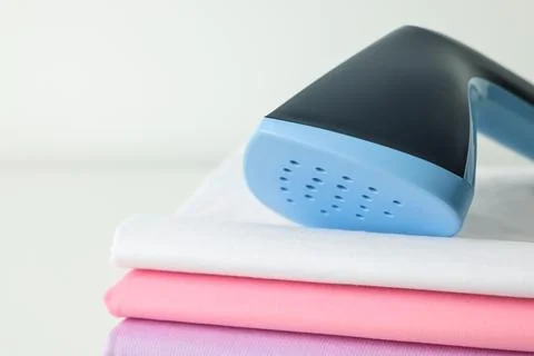 Upright steamer and stack of folded clothes on white table, closeup 스톡 사진