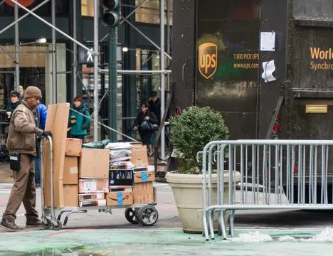 UPS driver loading packages onto a cart from back of truck Фото