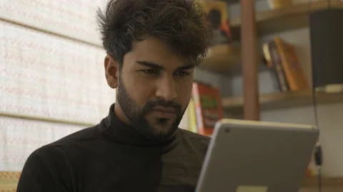 Upset Asian man using digital tablet while sitting on couch at home. Video stock 155197278