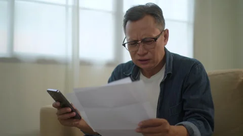 Upset asian senior man checking bills and paying with smartphone, older man. Stock Footage 265411570