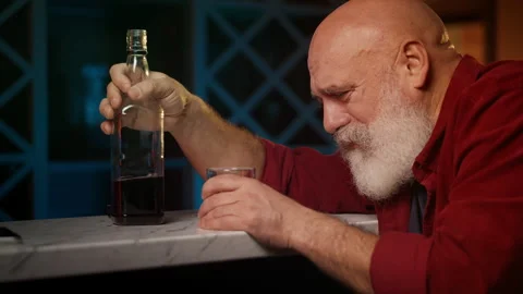 Upset bearded man in his 50s pours liquor into glass, coping with depression Stock Footage 346714115
