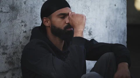 Upset Black man in durag sitting on rooftop, holding his head in a tense moment Stock Footage 331074481