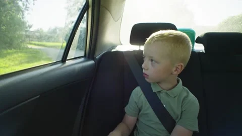 The upset boy looks out of the window in the back seat of the car with interest. Stock Footage 253393337