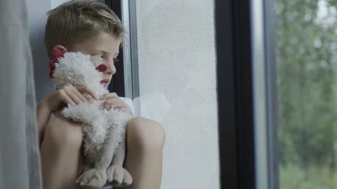 Upset Boy Sitting By The Window With Soft Toy In His Hands. Vídeos de archivo 135915444