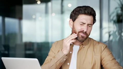 Upset businessman suffering from toothache while sitting at workplace at desk  Stock Footage 316677765
