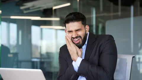 Upset businessman suffering from toothache while sitting at workplace in busines Stock Footage 334862028