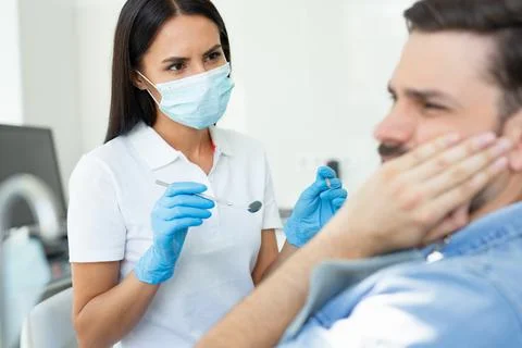 Upset client touching face while having toothache near dentist in the hospita Stock Photos