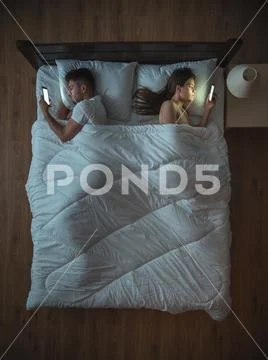 The upset couple with phone lie on the bed. view from above Stock Photos