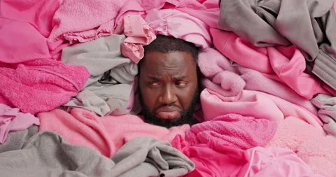 Upset dark skinned man drowned in laundry fees very upset surrounded by unfolded Vidéo 156633323