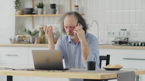 An upset elderly man talks on the phone at home in the kitchen, hears bad news Stock Footage 250163281