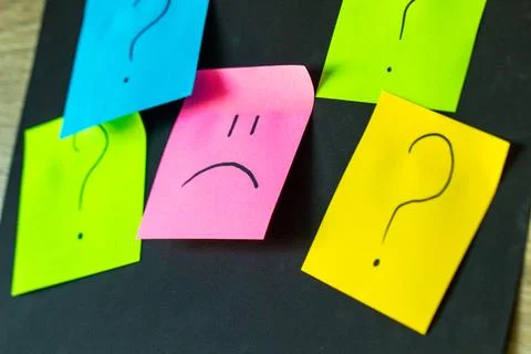 Upset emoticon surrounded by question marks on a dark background, failed attempt 库存照片