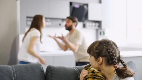 Upset girl sitting on the couch, while her parents fight at home in the kitchen Stock Photos