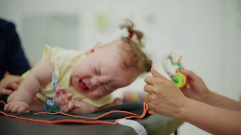 Upset infant baby crying, looking away from a person's hand holding a colorful Stock Footage 339810618