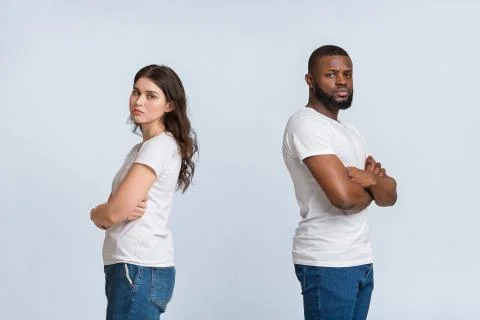 Upset interracial couple standing back to back with folded arms Stock Photos