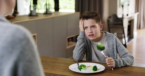 Upset little boy refusing to eat his broccoli while sitting at the kitchen table Vidéo 204760004