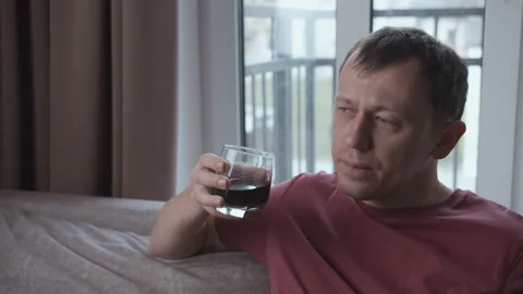 Upset man drinking alcohol while sitting on sofa, window background Stock Footage 159658679