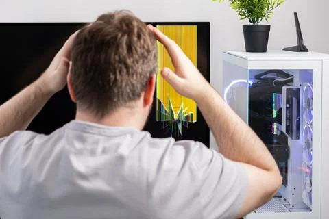 Upset man with hands on head seeing a broken computer monitor showing yello.. Stock Photos