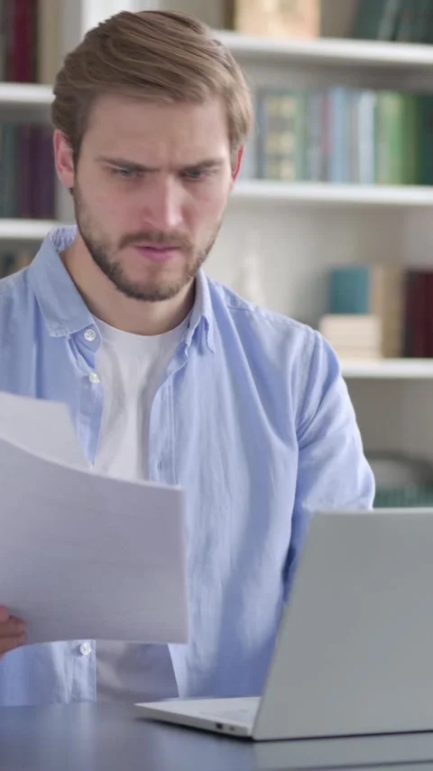 Upset Man Reading Documents while using Laptop, Vertical Video Vidéo 339578160