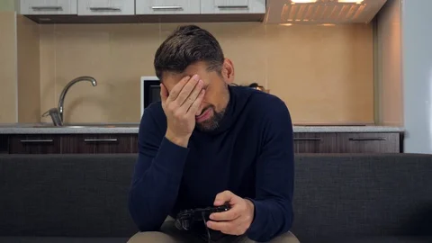Upset man is sitting on the couch, playing video game on console and losing Stock Footage 121842000
