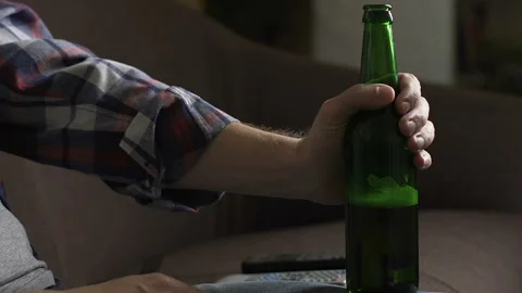 Upset man sitting on sofa, drinking beer and thinking about problems, failure Stock Footage 86784495