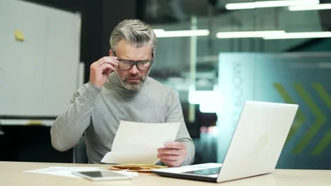 Upset mature gray haired bearded man in glasses reading letter with bad news  Stock Footage 232576520