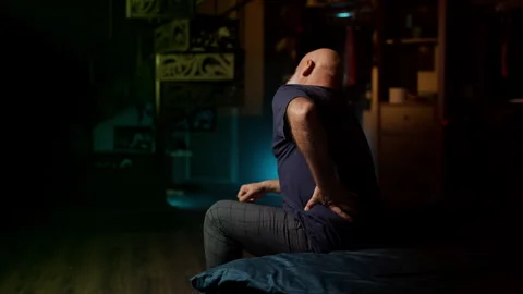 Upset middle-aged man feels sudden lower back pain while sitting on the sofa Stock Footage 342520767