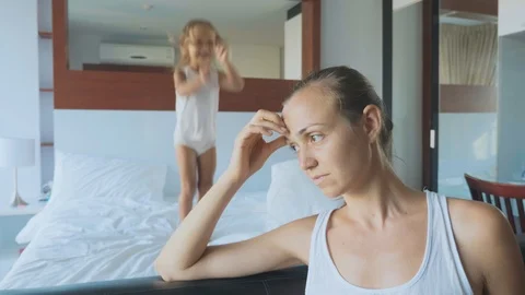 Upset mother with hyperactive child jumping on bed on the background Stock Footage 89743027