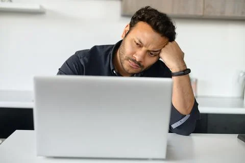 Upset multi-ethnic man is using laptop sitting at home alone Stock Photos