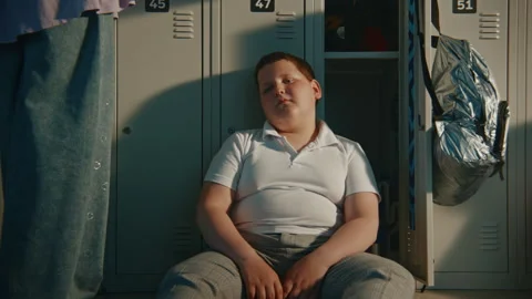 Upset Primary School Boy Sitting Alone on Hallway Floor beside Open Locker in Stock Footage 342022560