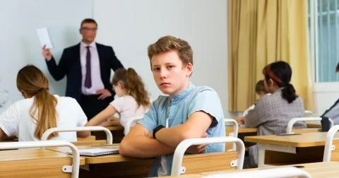 Upset teenage schoolboy sitting in classroom during lesson Stock Photos