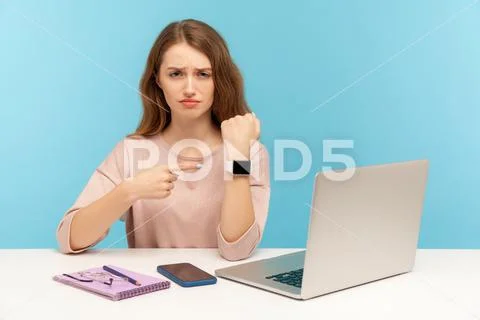 Upset tired woman employee sitting in office and pointing to watch on her han Stock Photos
