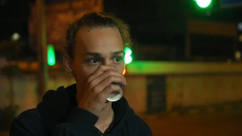 Upset young boy drinking tea on the bus stop in the city at night, 4k 動画素材 98502038