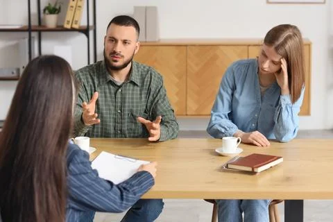 Upset young couple discussing problems with family mediator at table in offic Photos