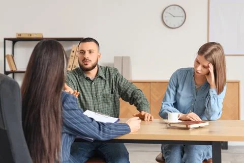 Upset young couple discussing problems with family mediator at table in offic Photos