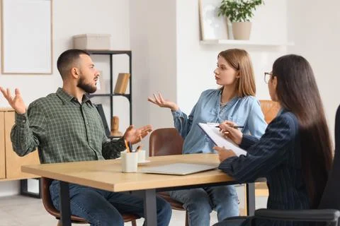 Upset young couple discussing problems with family mediator at table in offic Photos