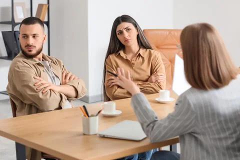 Upset young couple discussing problems with family mediator at table in offic Photos