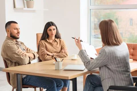 Upset young couple discussing problems with family mediator at table in offic Photos