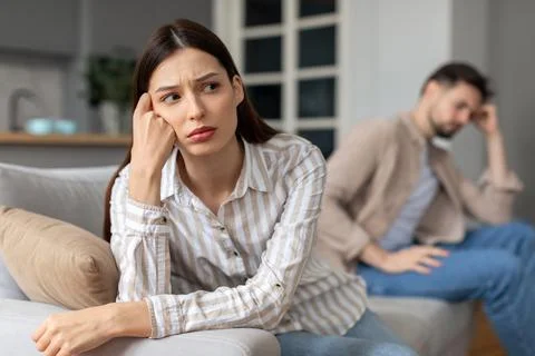 Upset young couple with problems sitting apart on sofa Foto stock