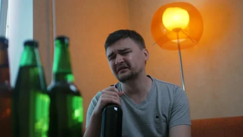 Upset young guy sitting on the sofa and drinking alcohol after brake up with gf  Stockbeeldmateriaal 197079471